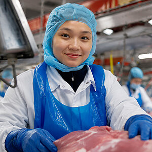 Nữ nhân viên mặc trang phục bảo hộ làm việc trong khu vực chế biến thịt.