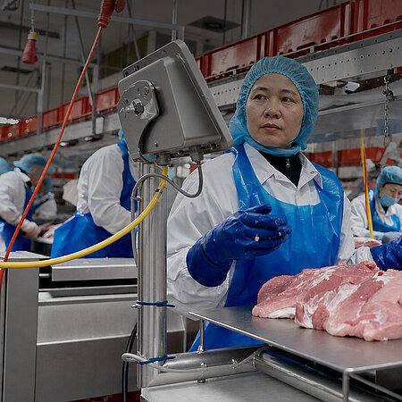 Nhân viên mặc trang phục bảo hộ làm việc tại dây chuyền chế biến thịt.