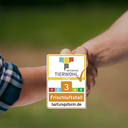 Zwei Menschen reichen sich die Hand, man sieht aber nur die Arme. In der unteren Bildmitte ist das Siegel für die Tierhaltungsform 3 zu sehen. 